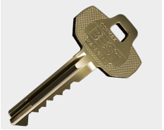 Brass house key with a hexagonal bow and jagged blade teeth, laid diagonally on a light background.