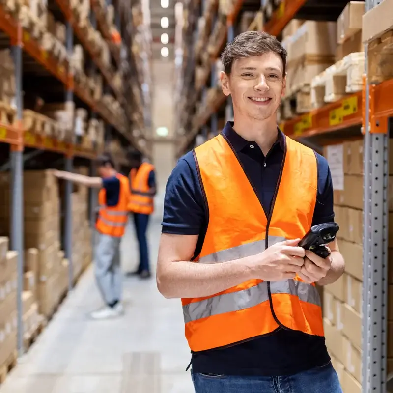 Smiling worker holds scanner in a warehouse aisle.